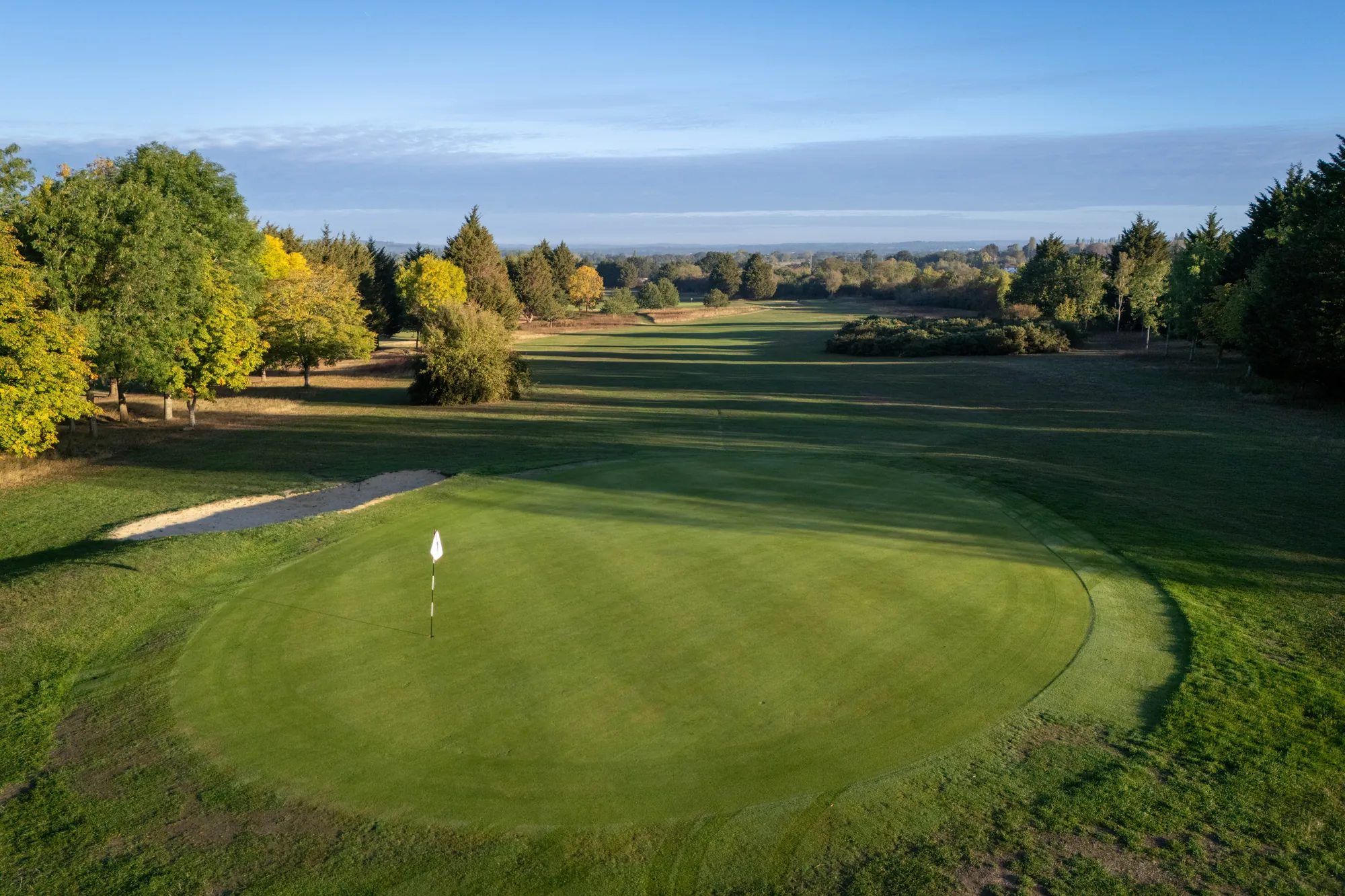 A green from the air with its flag, bunker and woodland behind, early morning