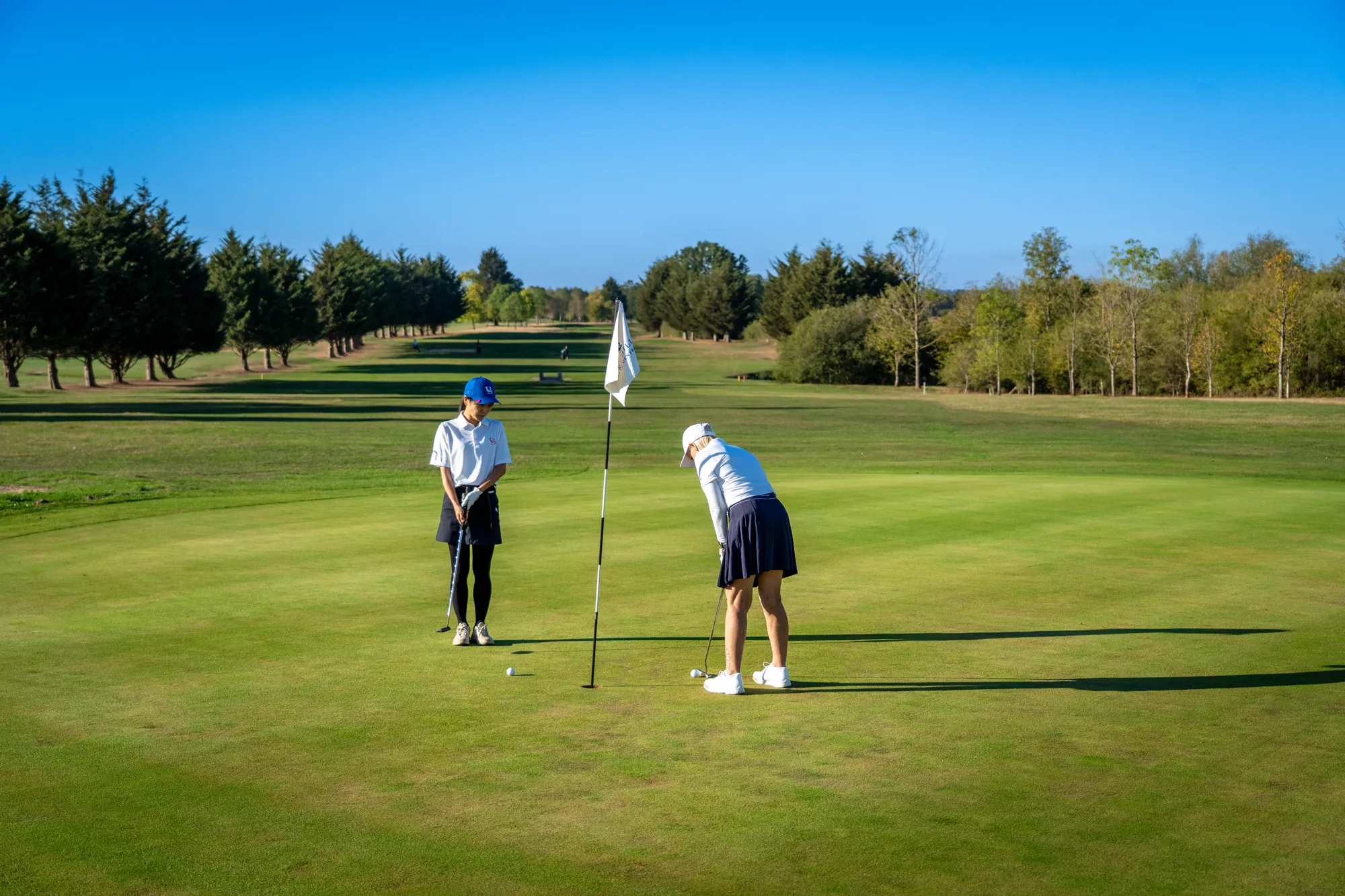 Two golfers on the green, one putting while the other holds the flag