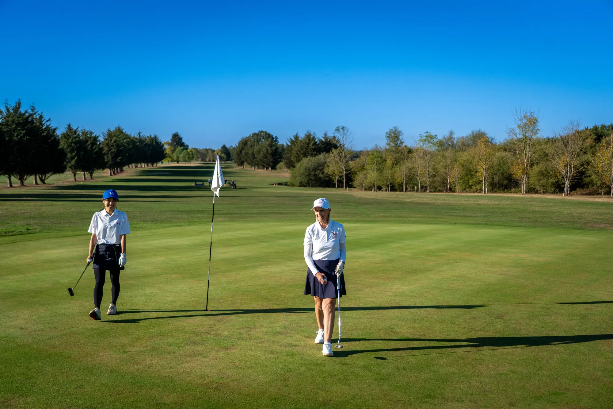 Two golfers on a green, one lining up a putt