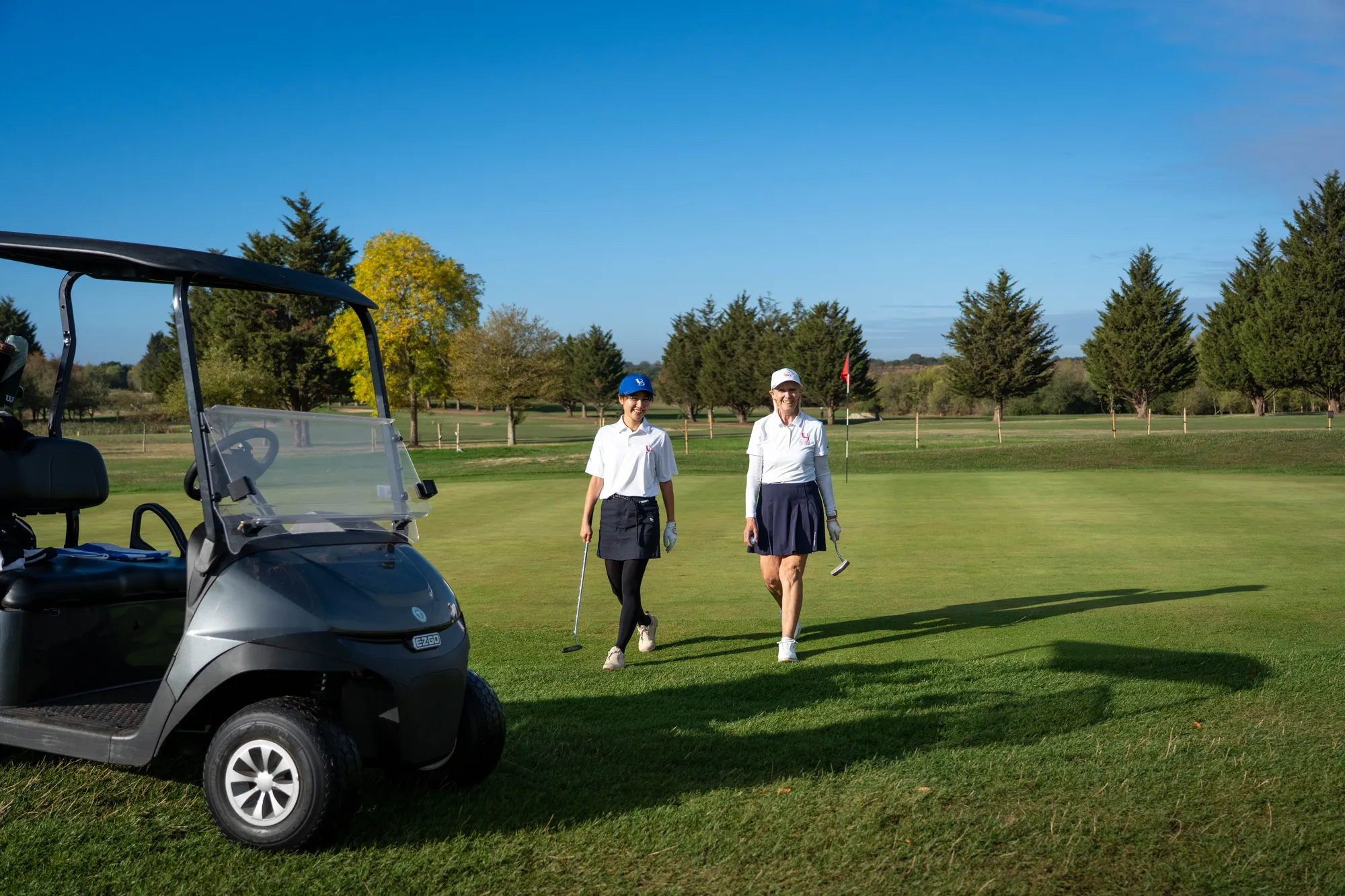 Two golfers walking across a green past their buggy