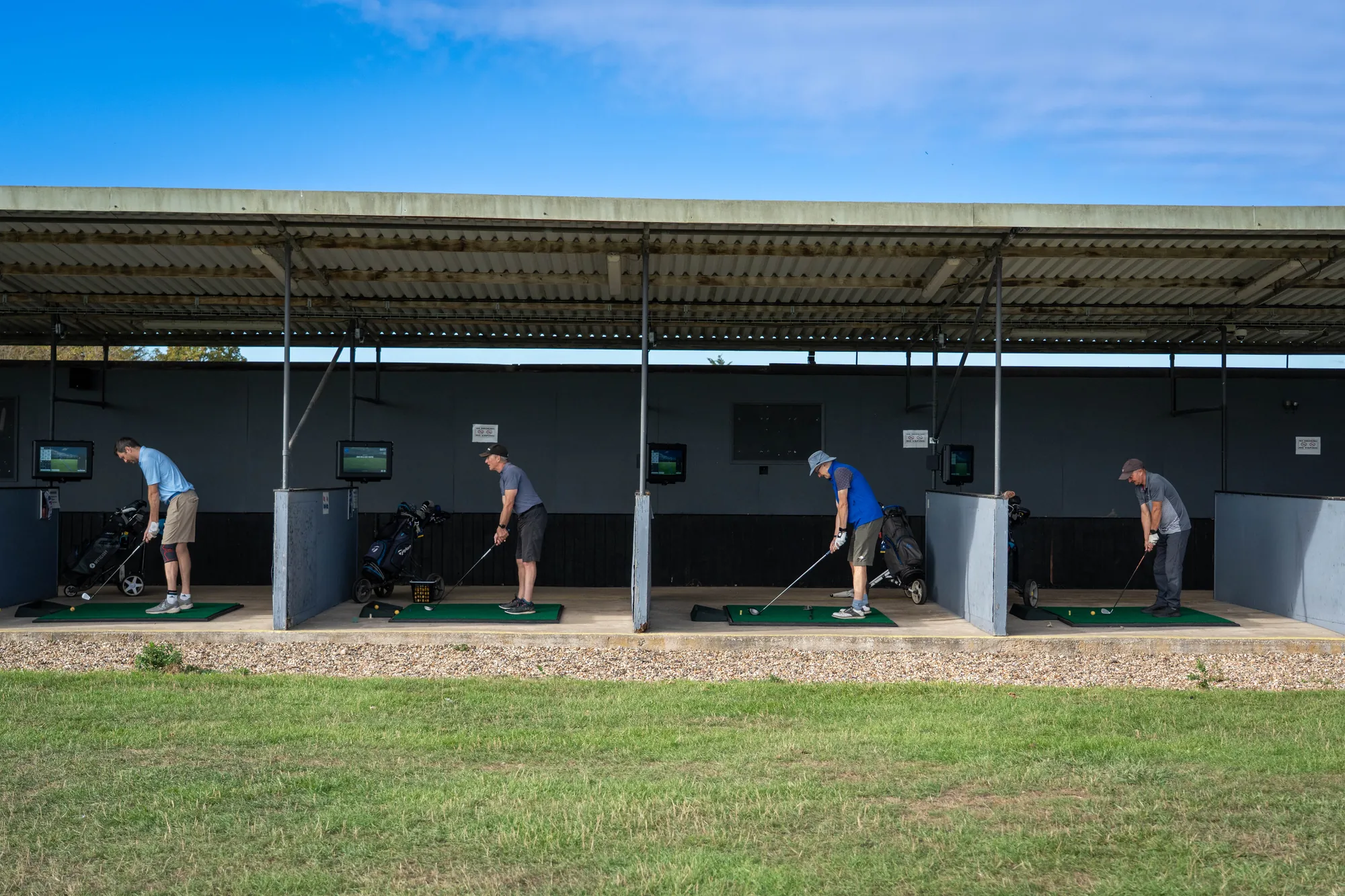 The covered range bays seen from the outfield, golfers mid-swing