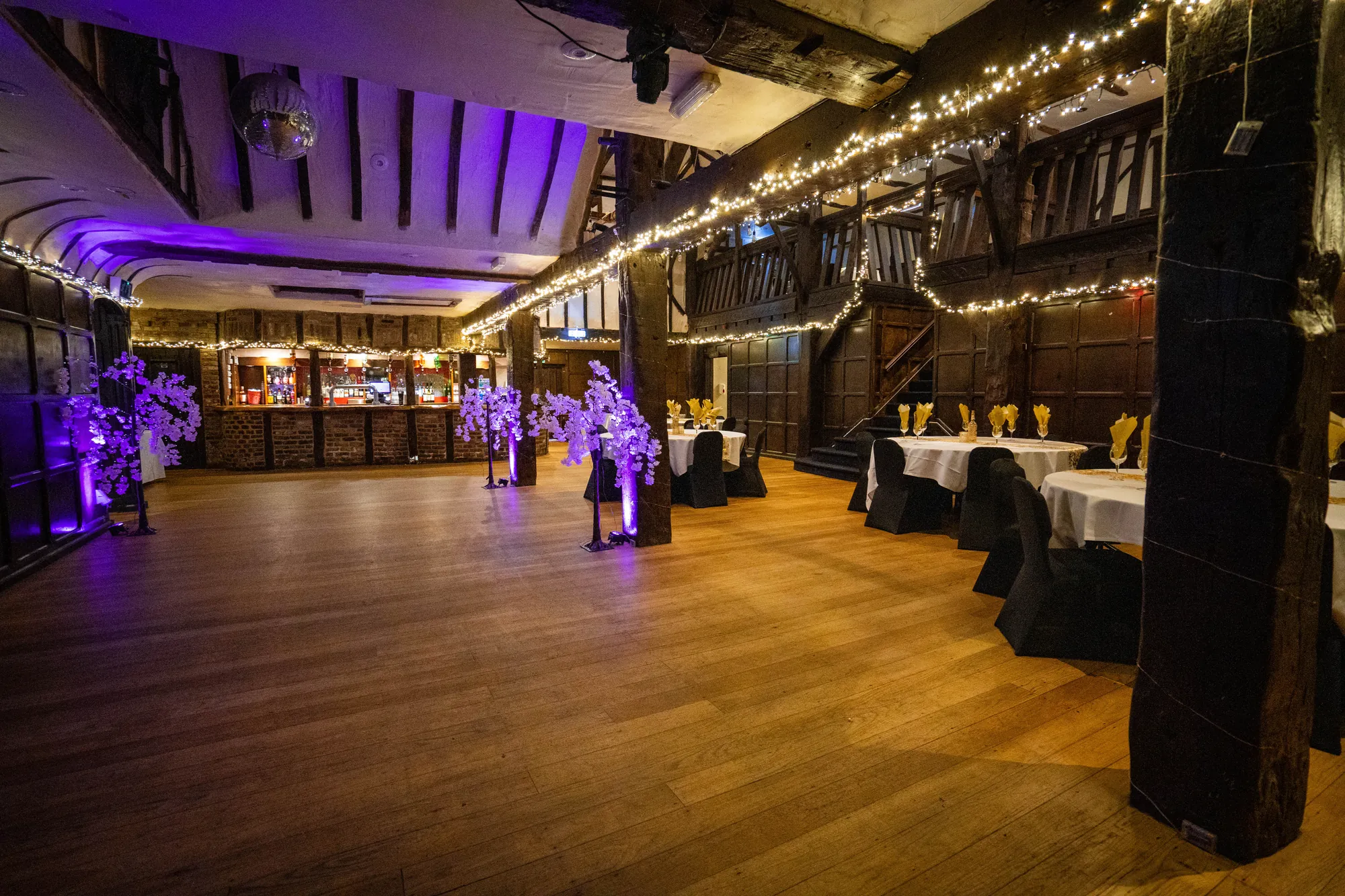The Baronial Hall dressed for a party, round tables and purple lights under the timber gallery