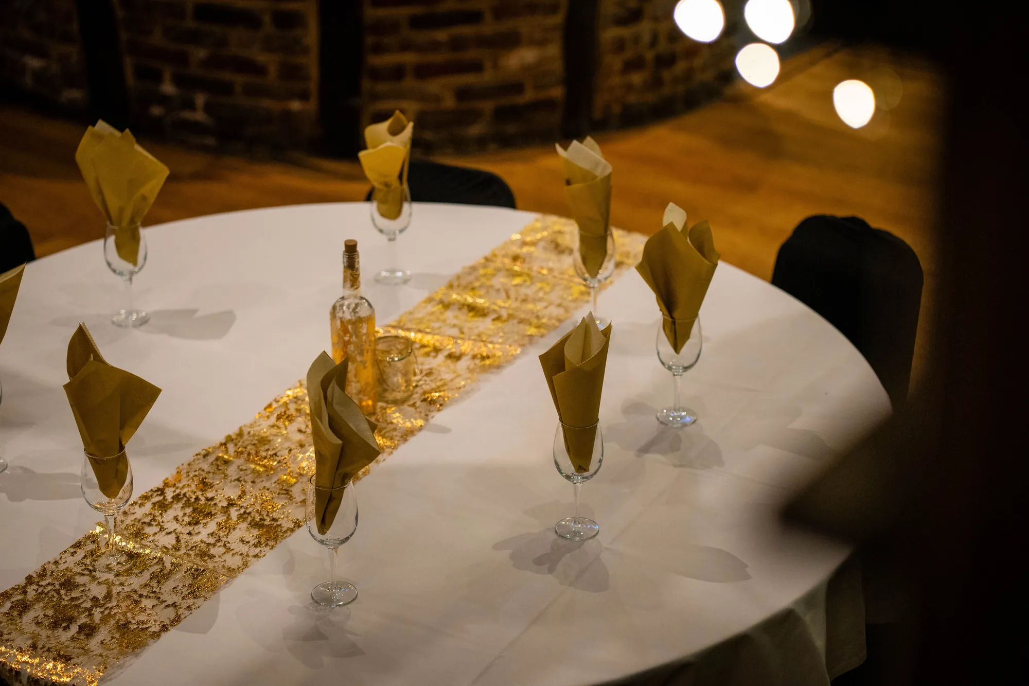 A round table set with gold napkins and a gold runner, warm lights blurred behind