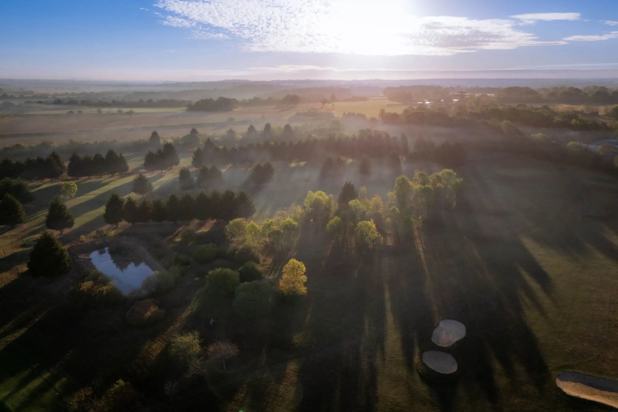 Morning mist over the pond and the countryside beyond, seen from the air at sunrise